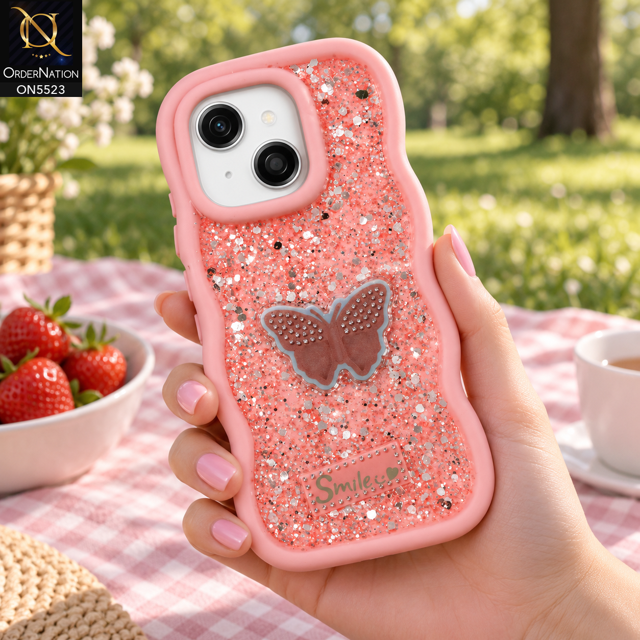 Tecno Pop 9 Cover - Pink - New Premium Smile Glitter Soft Case on the phone, held in a hand at a picnic (AI lifestyle render)